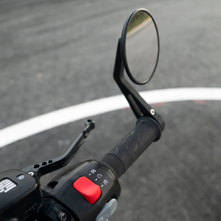 Close-up of a black BONVENT round bar-end mirror mounted above a motorcycle handlebar grip, shown beside the brake lever and controls.